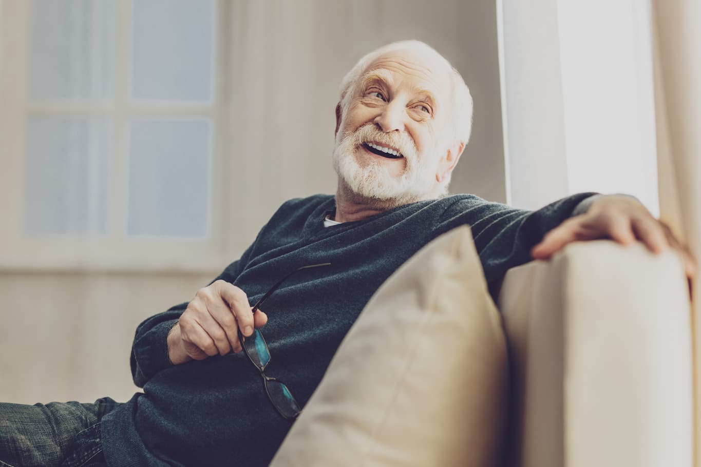 Senior man smiling while sitting on his couch and looking into the distance