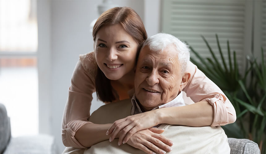 Smiling caregiver embraces an elderly man in a cozy living room.