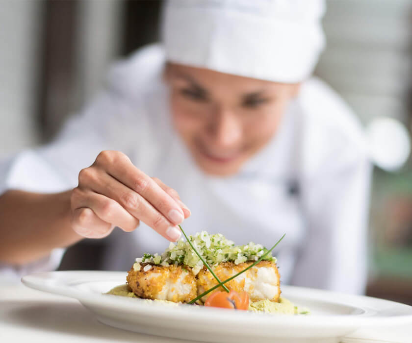 Chef garnishing a plated dish with fresh herbs and vegetables.