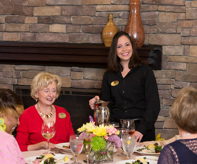 Smiling server pouring drinks for residents at dining table in a community setting.