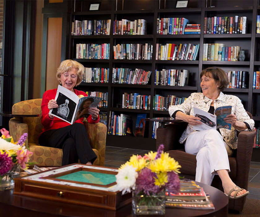 Two women reading magazines in a library at a senior living community.