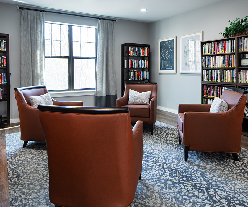 Cozy reading area with leather chairs, bookshelves, and artwork in a living community.