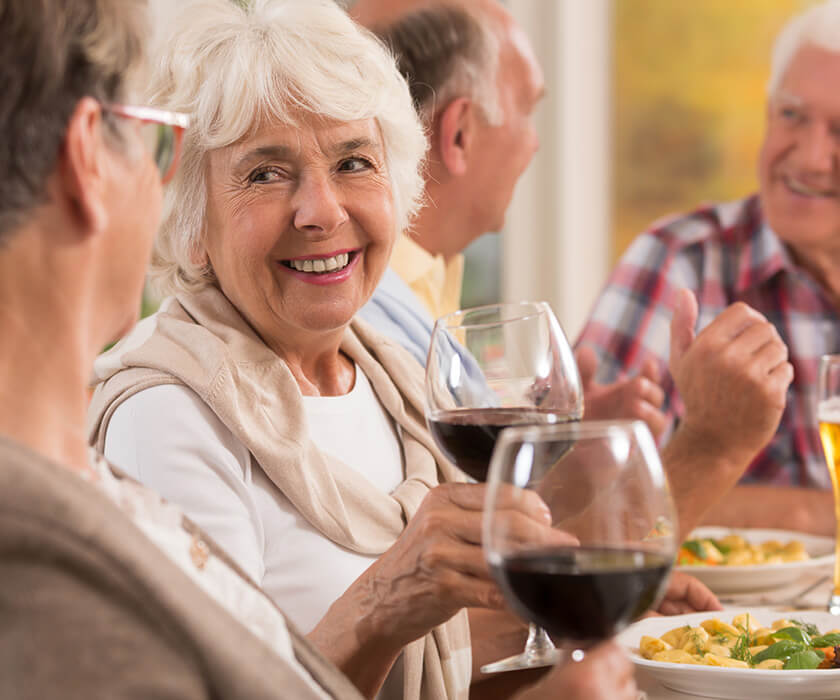 Seniors enjoying a meal and wine, engaged in lively conversation.