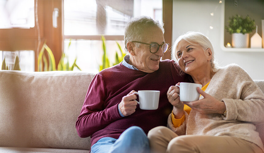 Elderly couple enjoying coffee together on a cozy sofa in a bright living room.