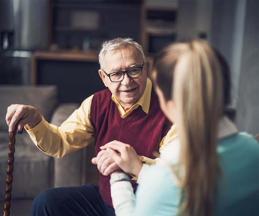 Elderly man with cane talks to caregiver in a senior living unit.