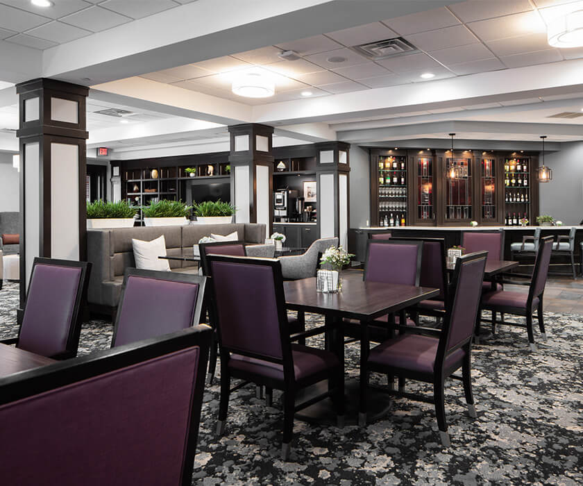 Elegant dining area with purple chairs, dark wood tables, and a wine display in background.