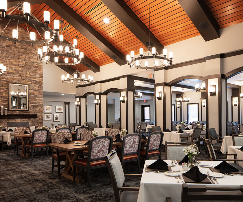Elegant dining room with chandeliers and stone fireplace in a senior living community.