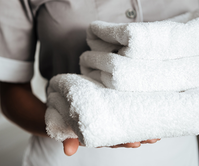 Person holding neatly folded white towels in a senior living unit.