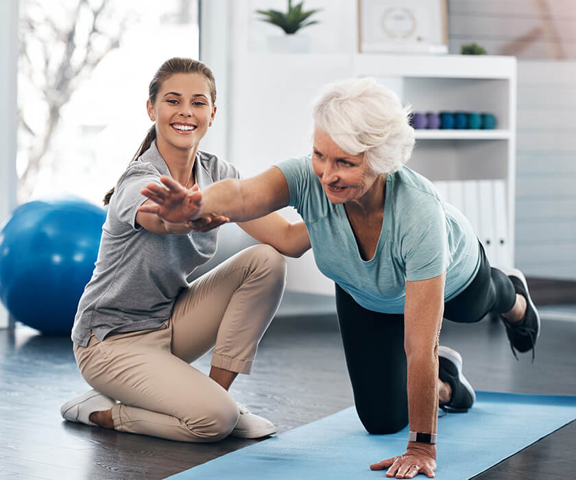 Elderly woman exercising with a young trainer in a bright studio.
