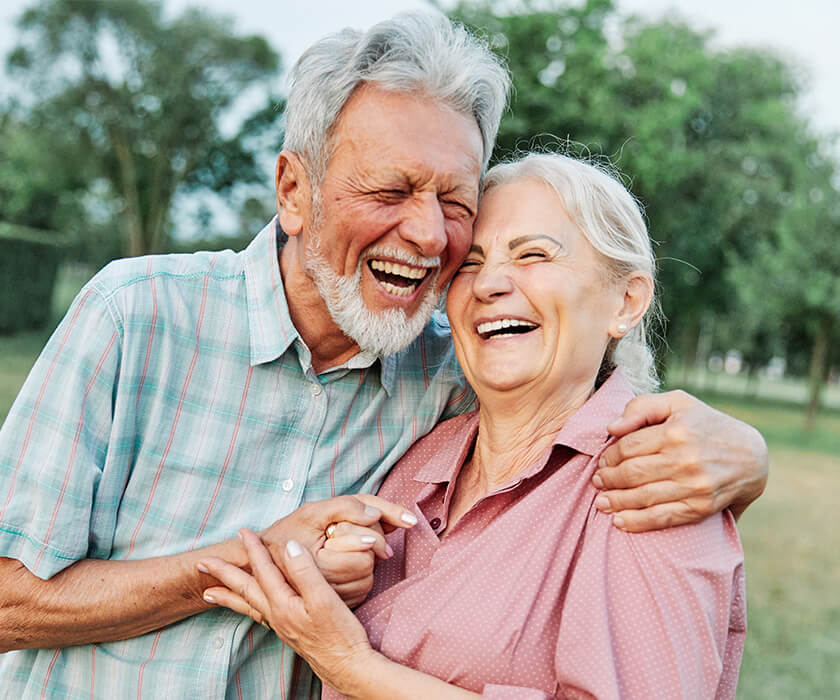 Smiling elderly couple embracing in a park during a sunny day.