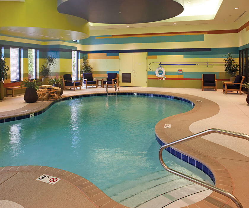 Indoor swimming pool area with colorful walls and seating in a senior living community.