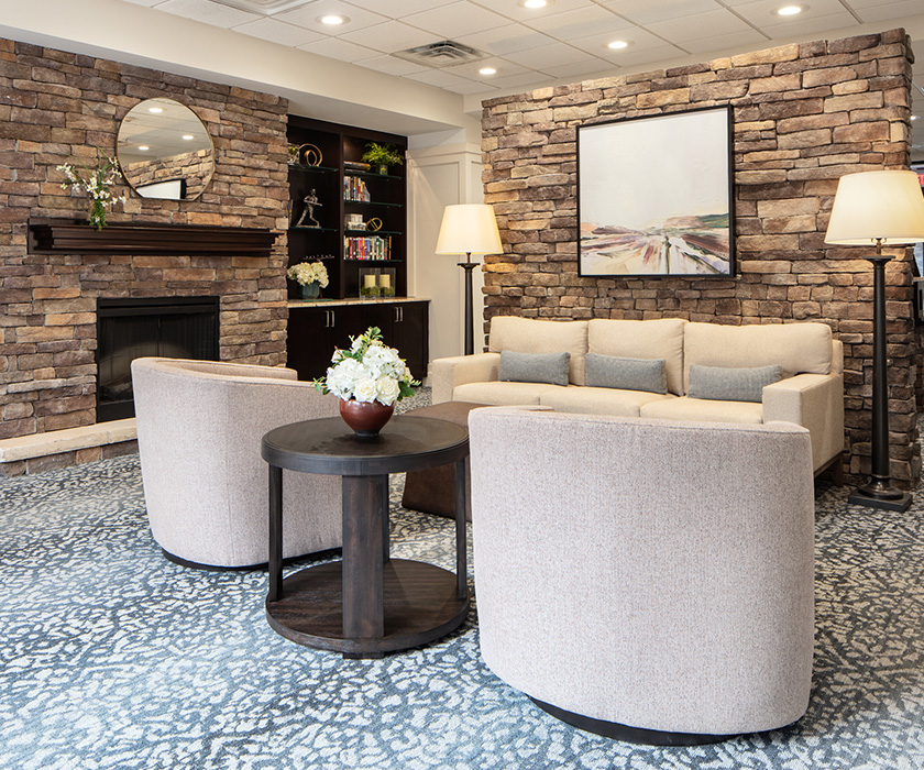 Cozy seating area with beige sofa, armchairs, and stone fireplace in community lounge.