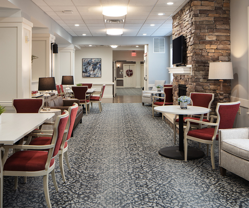Spacious lounge area with red chairs and a stone fireplace in a senior living community.