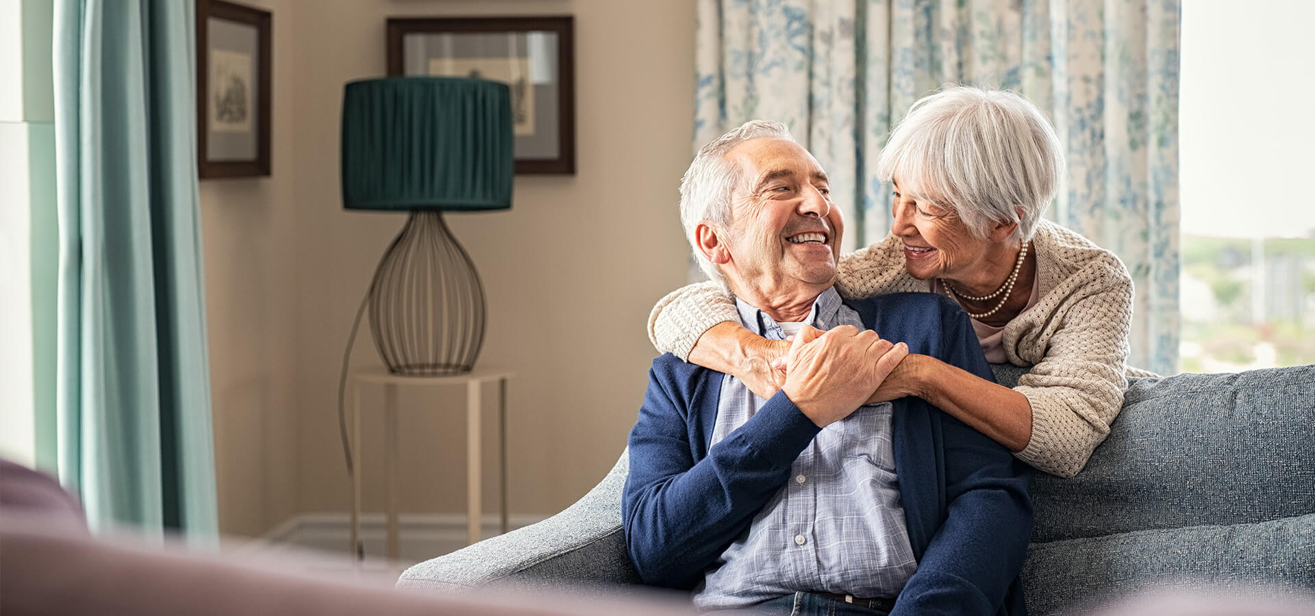 Smiling elderly couple embracing on a cozy couch in a well-lit living room.