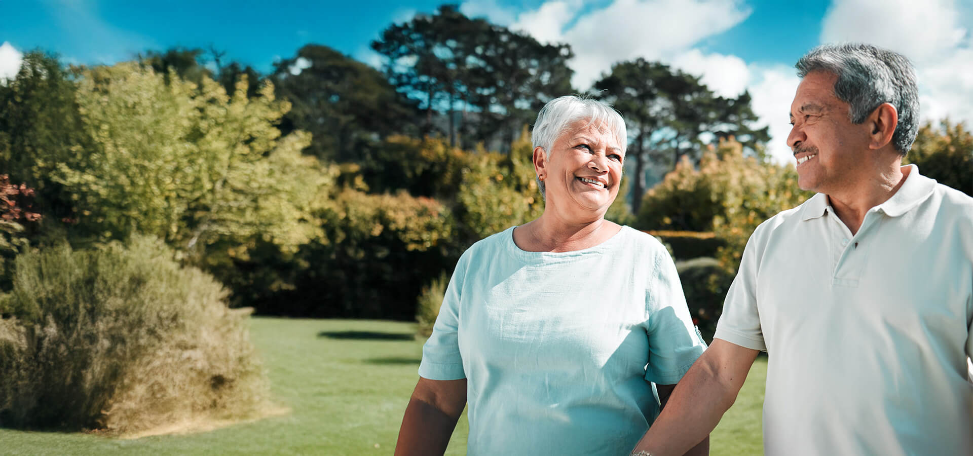 Smiling senior couple walking outdoors in a lush green garden setting.