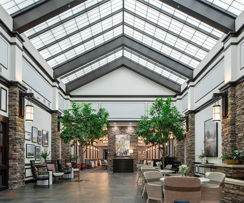 Spacious lobby with skylights, seating areas, and indoor plants in a modern community building.