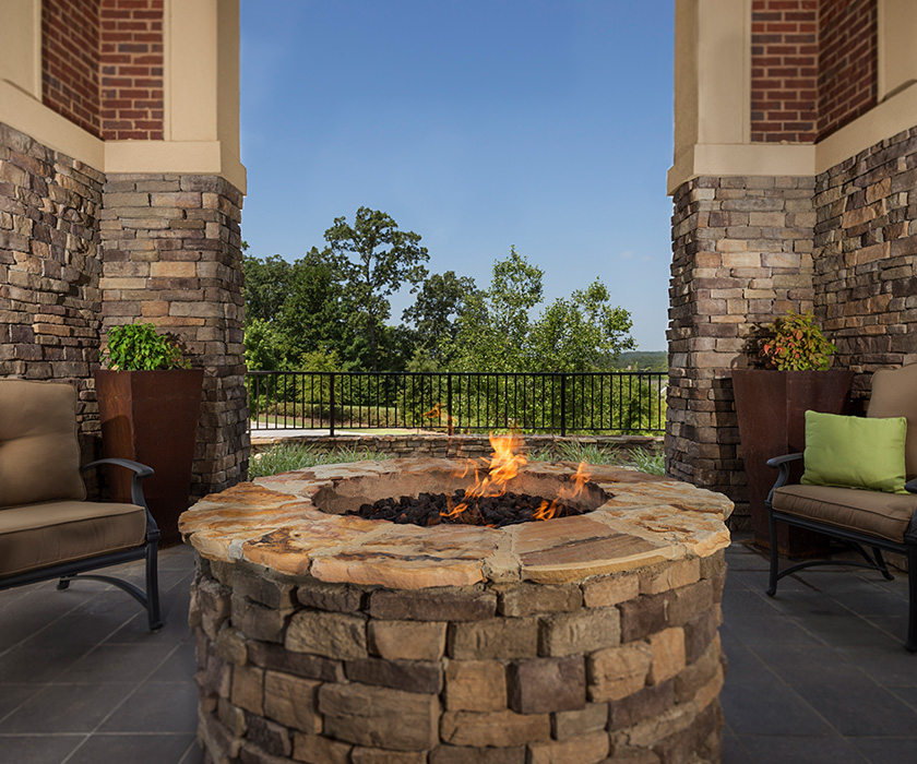Outdoor patio with stone fire pit and cozy seating, surrounded by trees.