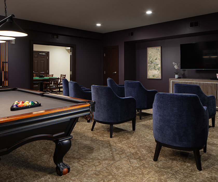 Recreation room with pool table and blue chairs in a senior living community.