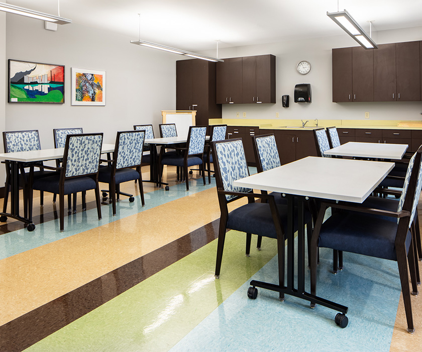 Dining area with tables and chairs in a senior communitys communal space.