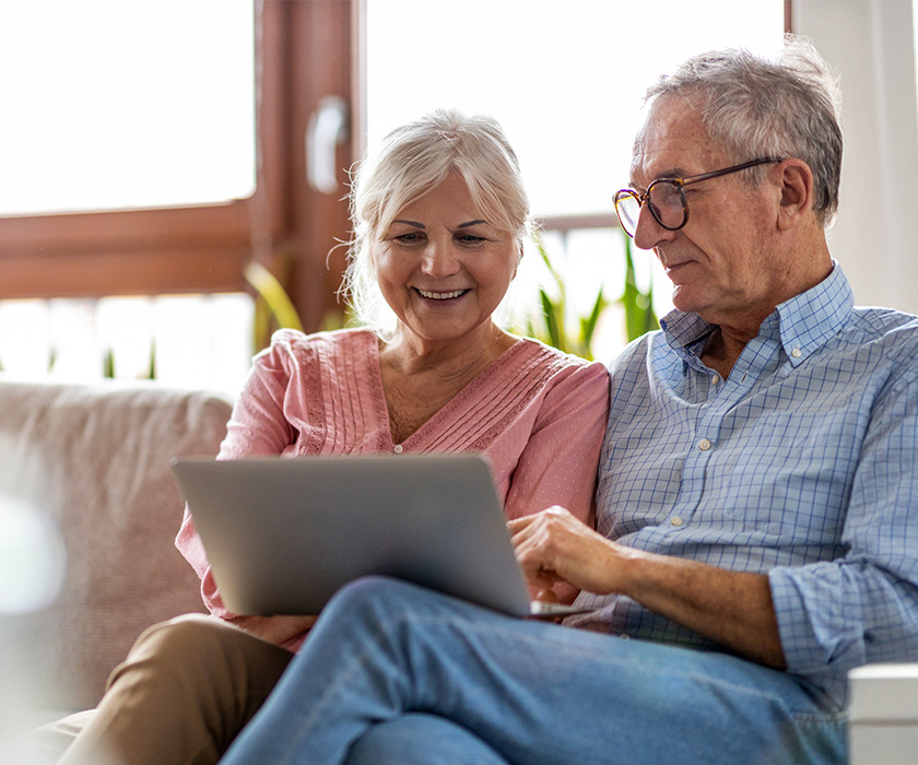 Smiling senior couple sitting on a sofa looking at a laptop together.