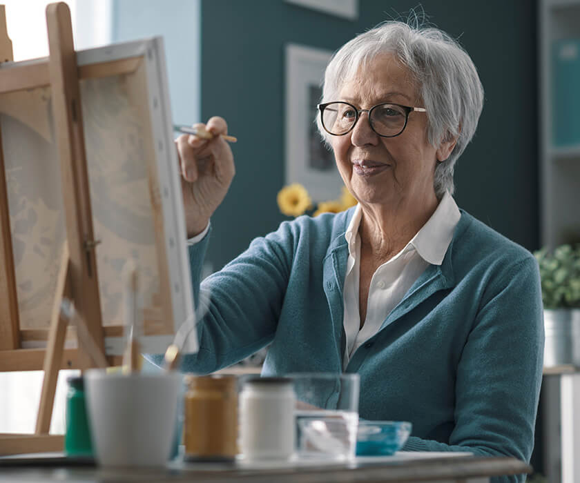 Senior woman painting at an easel in a comfortable living space.