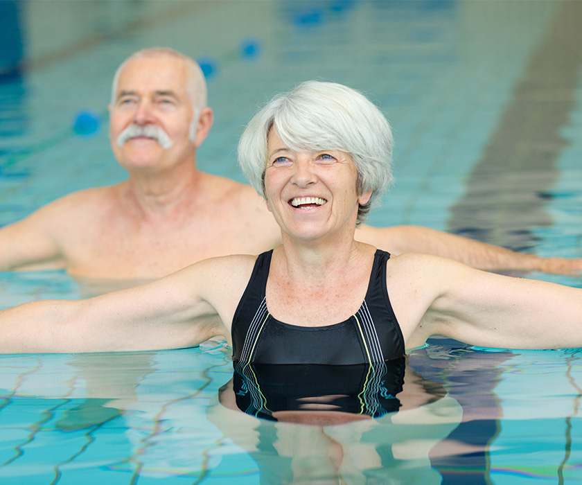 Two happy seniors enjoying water exercise in an indoor pool.