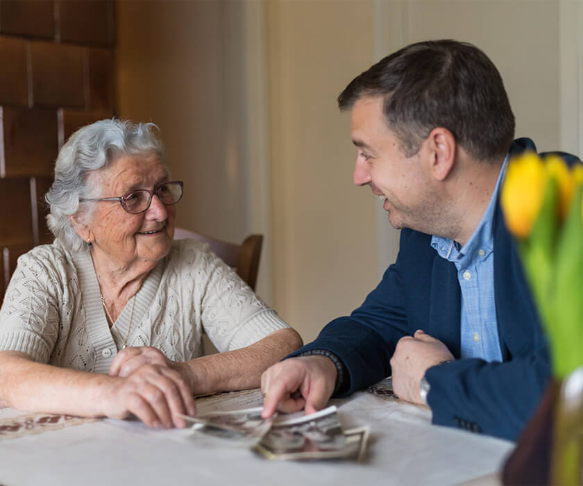 Elderly woman and man smiling, looking at photographs on a table in cozy setting.