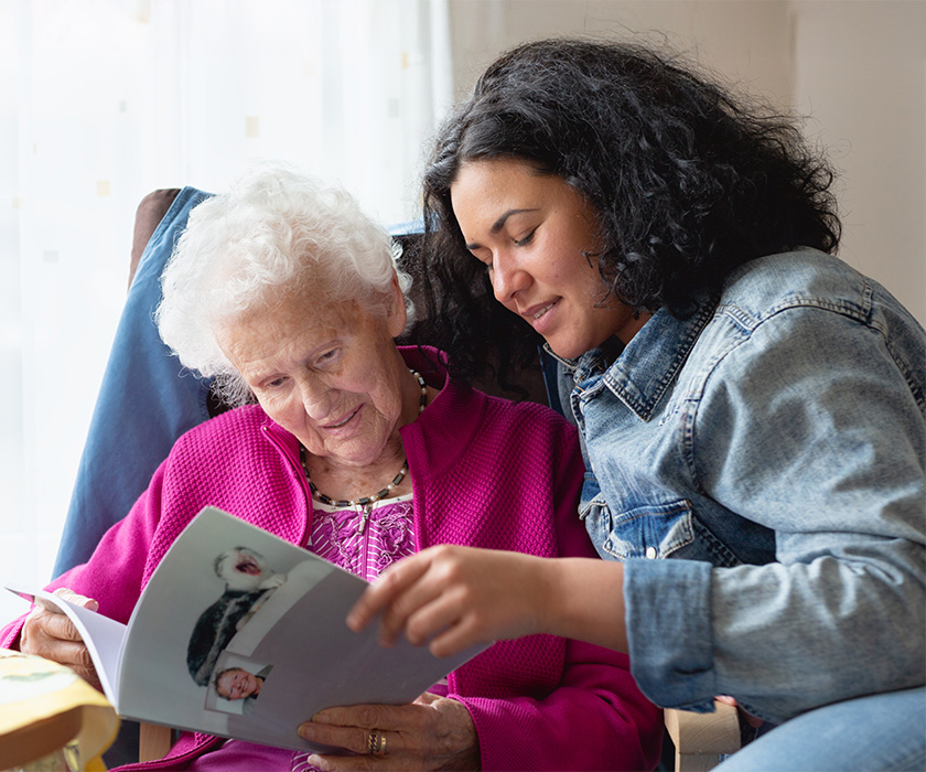 Elderly woman and younger woman looking at a photo album together.