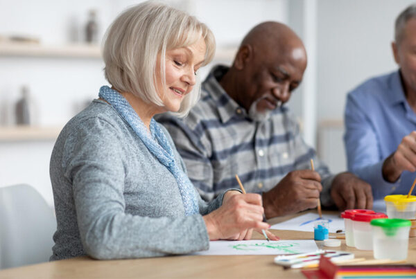 Woman smiling as she and two men paint pictures at a table