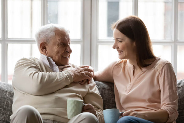 Elderly man and young woman smiling while sitting on a sofa, holding mugs